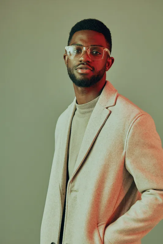 Stylish portrait of a fashionable Black man in a beige coat, expressing confidence with a neutral background and a warm color palette, ideal for showcasing modern fashion trends