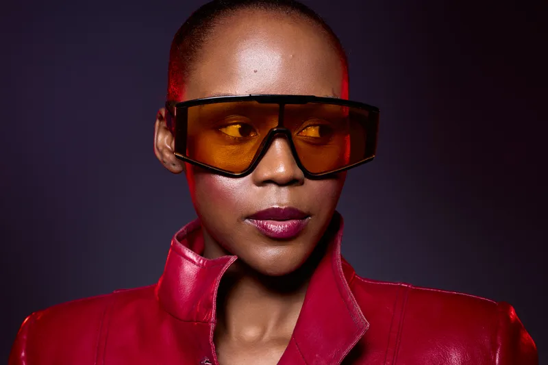 Close-up of a dark skinned African woman wearing oversized orange sunglasses and a red leather jacket. Studio portrait with dramatic lighting and modern fashion concept.