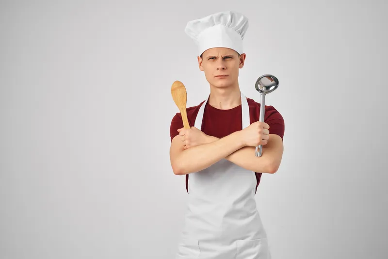 Повар-мужчина в белом фартуке, кухонная утварь, приготовление изысканной еды