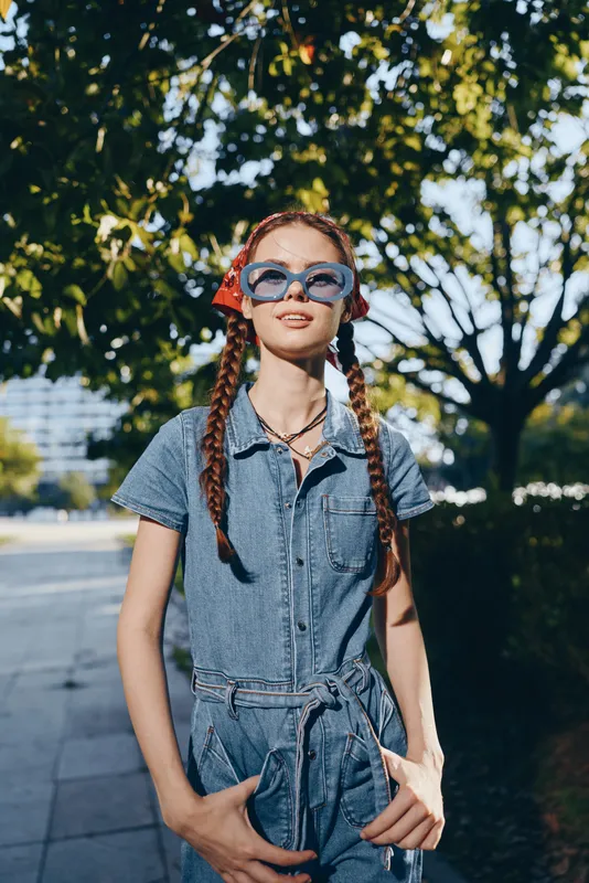 lifestyle woman in modern boho-western denim street style with sunglasses and braids, confident and stylish outdoors, film color tones enhancing natural light and shadows