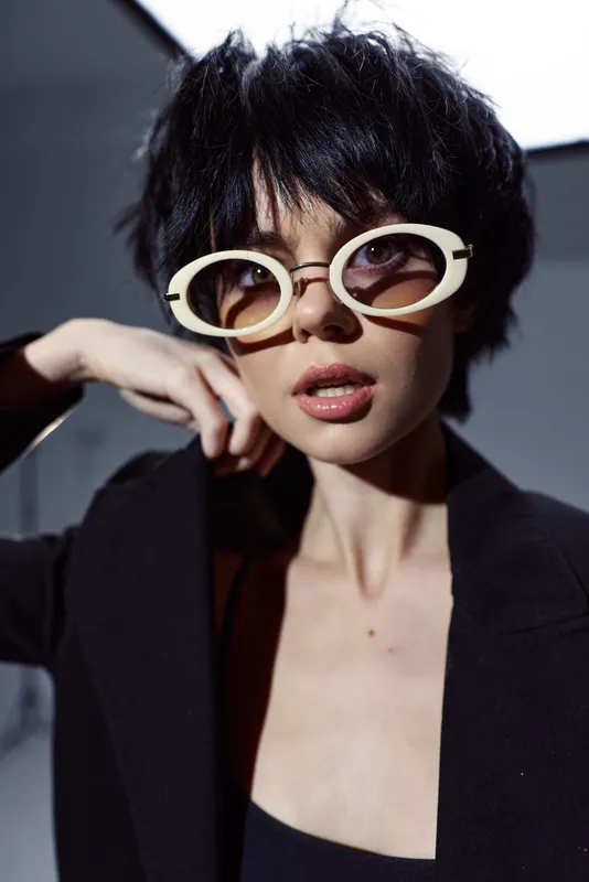 Stylish woman with short black hair wearing retro sunglasses and a black blazer looking confident in a modern setting
