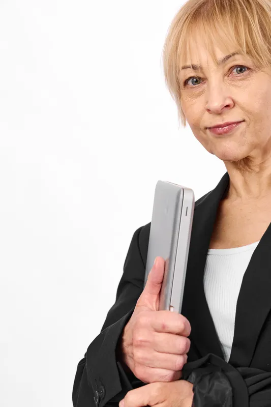 Senior woman portrait in studio, holding smartphone in hand, serious expression on a white background, concept of communication and technology for aging.