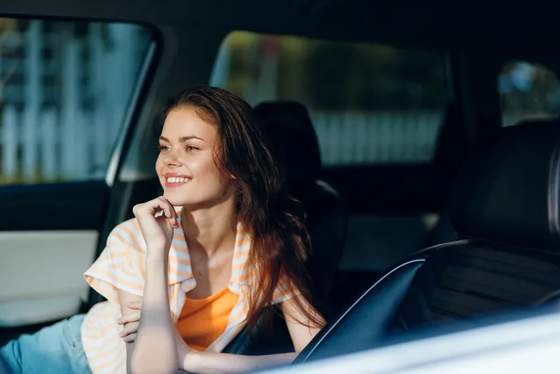 Молодая женщина с длинными волосами улыбается, сидя в автомобиле