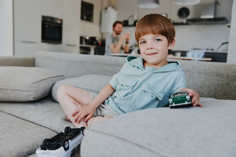A little boy playing with toy cars on a cozy sofa, showcasing a cheerful expression and a relaxed environment. Ideal for family and childhood themes.