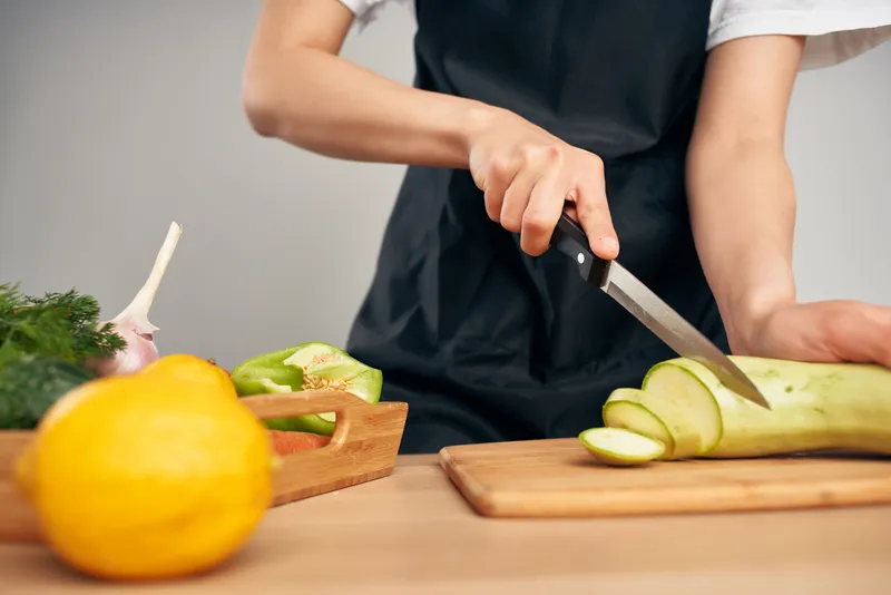 Женщина в черном фартуке нарезает овощи на кухне, готовя еду