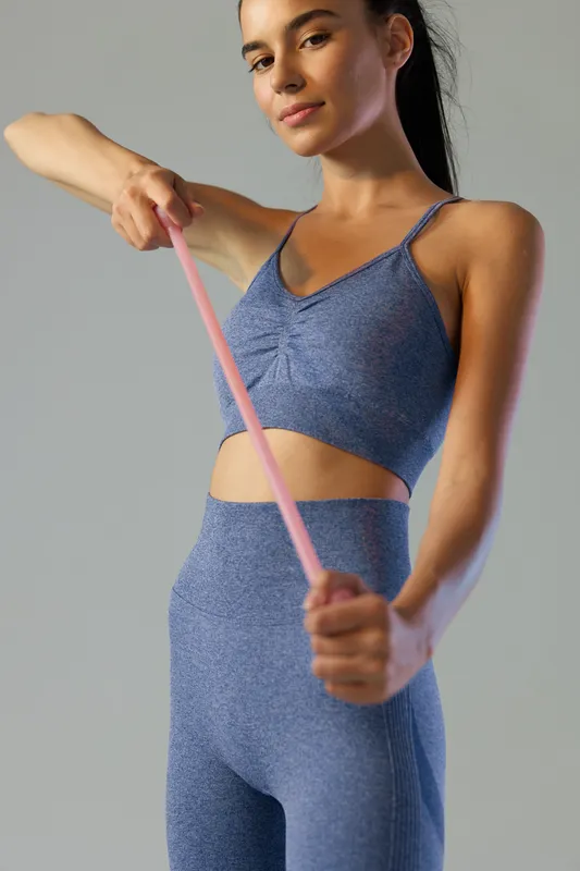 Young woman sport fitness exercising with resistance band wearing blue seamless activewear, focused and healthy lifestyle concept in simple gray studio background.