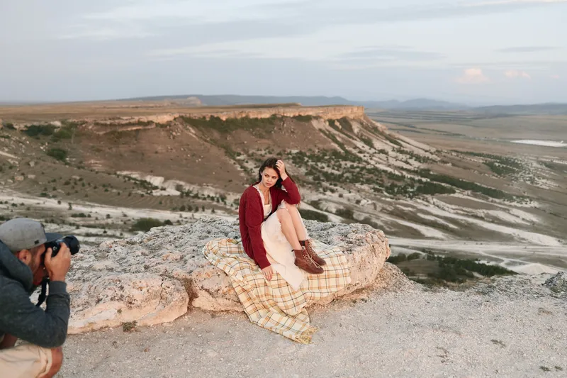 Горное приключение: мужчина фотографирует женщину на краю скалы на фоне величественных гор