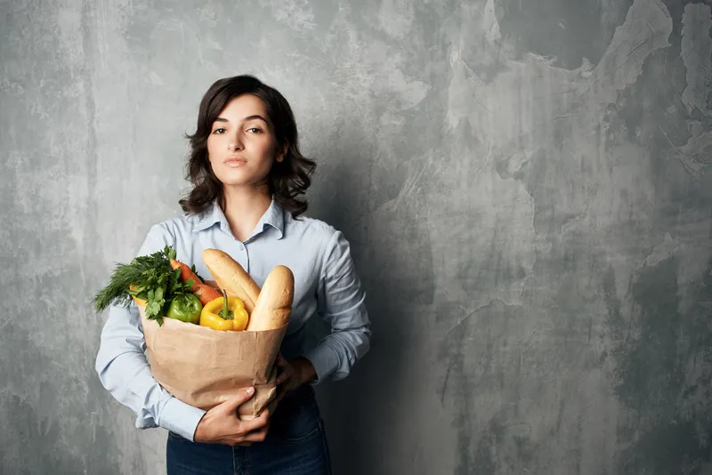 Женщина с пакетом продуктов, в котором лежат овощи