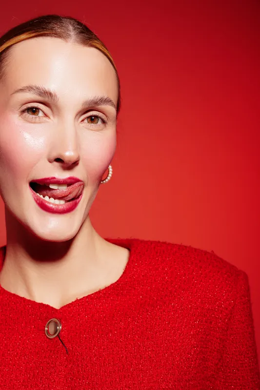 Close-up of a smiling woman with glossy skin and red lipstick wearing a red top against a red background. Concept of beauty, fashion, makeup, and confident expression.
