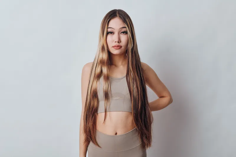 Woman with long hair wearing casual sleeveless top and pants standing against white background. Front view, confident pose with natural makeup and relaxed expression.