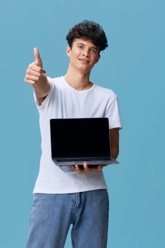 young man showing laptop and thumbs up gesture, casual clothing, smiling expression, blue background, positive and modern technology concept