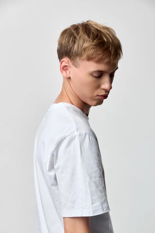 Boy, side profile, white t-shirt, youth, studio, casual wear, male, young, serene, minimal with calm posture and clean lighting in a neutral background