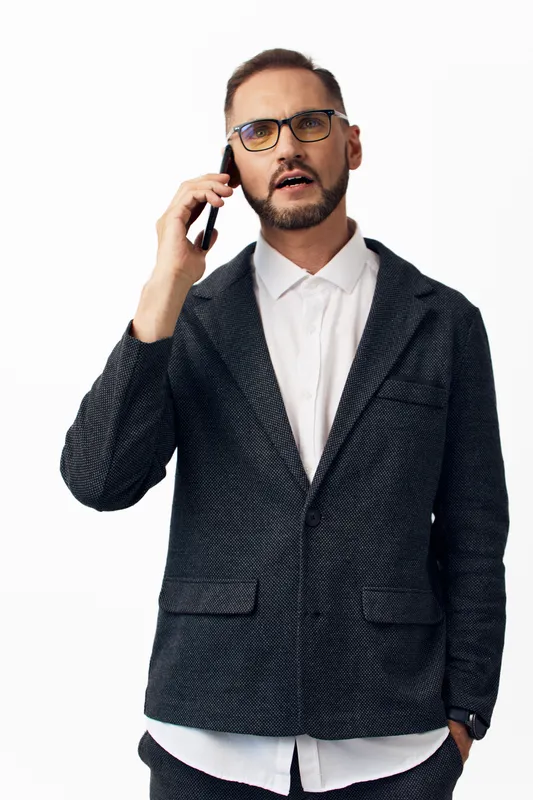 A professional man on a colorful isolated background, wearing a smart blazer and glasses, talking on a mobile phone with a confident expression, showcasing a dynamic business moment.