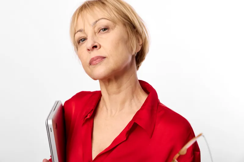 Senior woman with short blonde hair holding a smartphone tablet, red blouse in studio on white background, focused portrait, technology communication concept, soft light calm