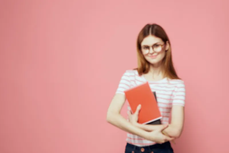 Красивая студентка держит книги, жестикулирует руками на розовом фоне