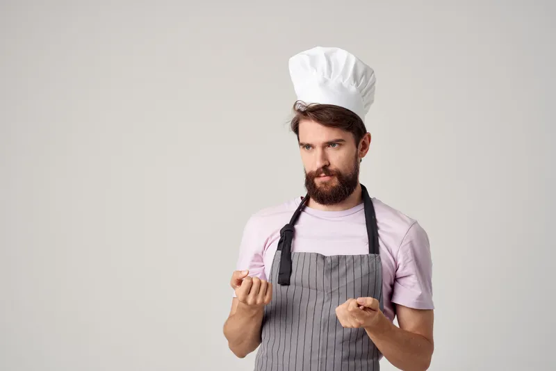 Мужчина в поварском колпаке и фартуке работает поваром на кухне ресторана