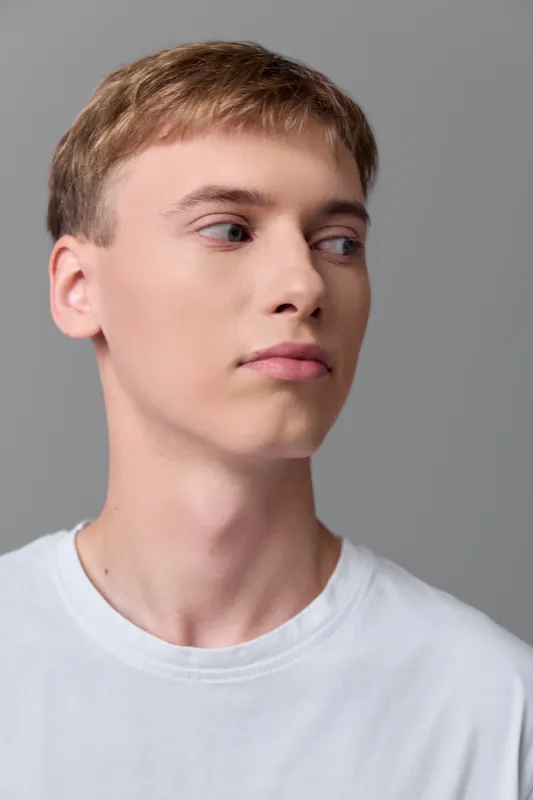Young man in a white T shirt captured in side profile with a neutral expression, studio lighting and a clean backdrop, minimalist image suitable for fashion, lifestyle, or editorial use