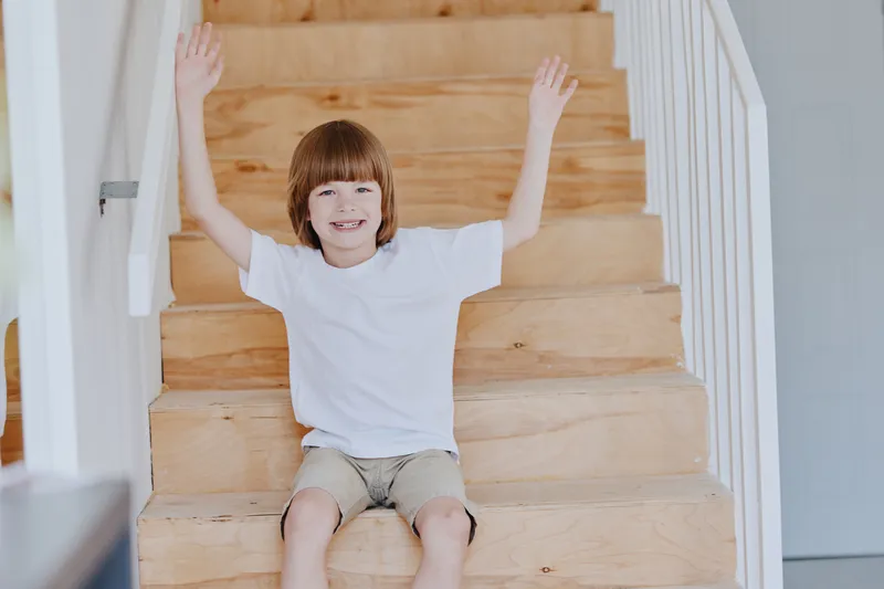 Cheerful boy sitting on wooden stairs, enjoying a playful moment. His joyful expression and casual outfit create a delightful atmosphere.