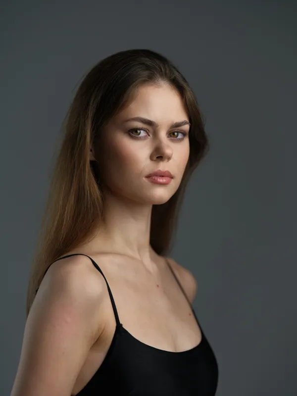 young woman with long hair wearing black top looking at camera with serious expression