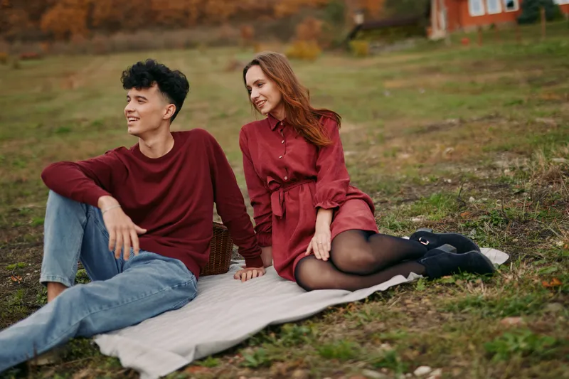 A candid scene of a young couple resting on a blanket in a park, conveying authenticity and trust through natural smiles and effortless connection.