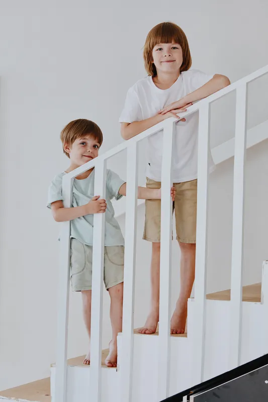 Two playful boys standing on a staircase, wearing casual outfits, showcasing a cheerful atmosphere in a modern home setting. Perfect for lifestyle content.