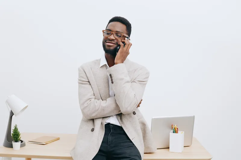 Smiling man wearing glasses and casual neutral blazer pose indoors at workplace with white background. Confident, professional, cheerful, relaxed, modern, workspace, light. Concept: workplace success.
