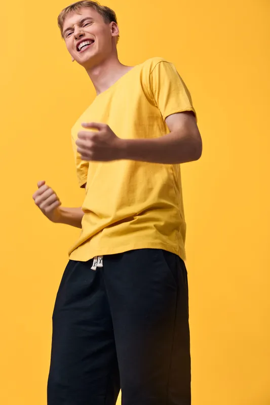 Smiling man wearing a bright yellow shirt in a bold monochrome backdrop, casual pose conveying joy, energy and confident street style for lifestyle and fashion focused imagery