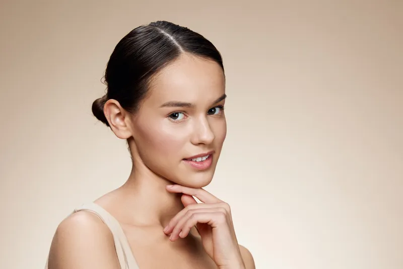 Natural beauty portrait of a young woman with a serene expression, featuring soft lighting and a neutral background, ideal for wellness and beauty themes