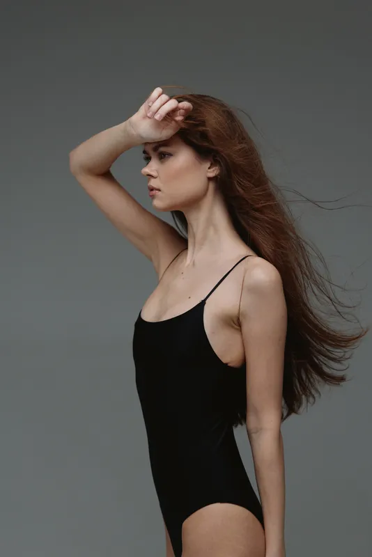 Profile of a young woman in a black bodysuit shielding her eyes with her hand, showing natural pose and neutral expression.
