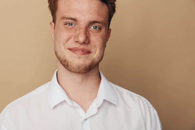 Portrait of a smiling young man with red hair and freckles wearing a white shirt against a beige background. Concept of confidence, natural beauty, and casual lifestyle.