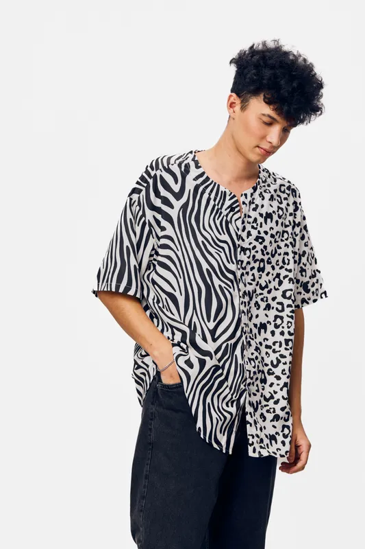 young man wearing a striking black and white animal print shirt, standing against a plain white background with a casual and contemplative expression