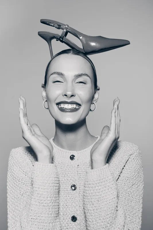 Happy Caucasian woman with light skin wears high heel shoe on head smiling with closed eyes in studio portrait.