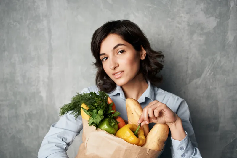 Весёлая женщина с пакетом продуктов, совершающая покупки овощей в супермаркете