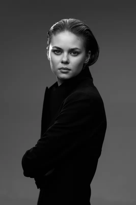 Black and white portrait of a serious woman in black clothing with crossed arms and intense gaze