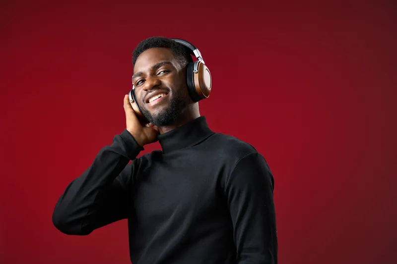 Smiling African man enjoying music with headphones against a vibrant red background, embodying happiness, with a focus on modern style and emotional connection