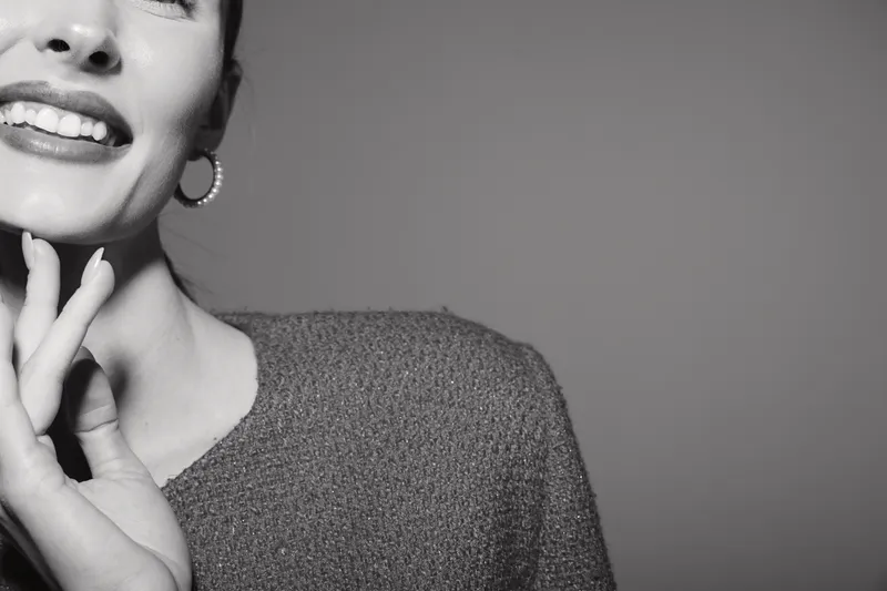 Closeup of smiling caucasian woman with fair skin wearing earrings and textured sweater on neutral background. Concept for happiness, beauty, and positive emotions.