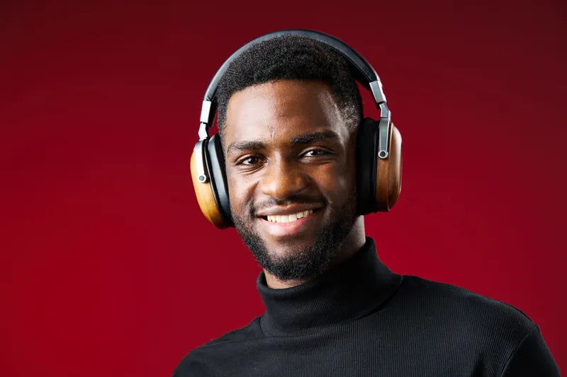 Smiling young African man wearing stylish headphones, enjoying music with a red background, conveying joy and relaxation through modern lifestyle imagery