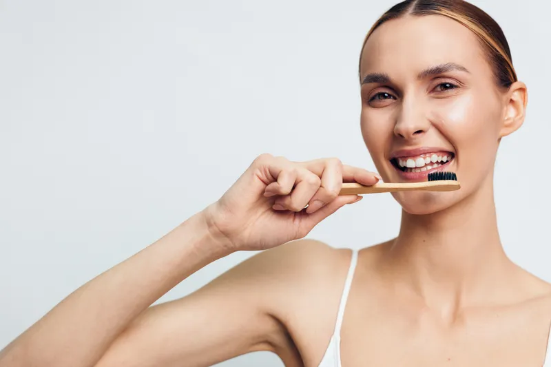 Young woman with light hair brushes her teeth with a toothbrush against a clean white background, conveying a fresh morning dental routine, her expression bright and relaxed as she focuses on proper