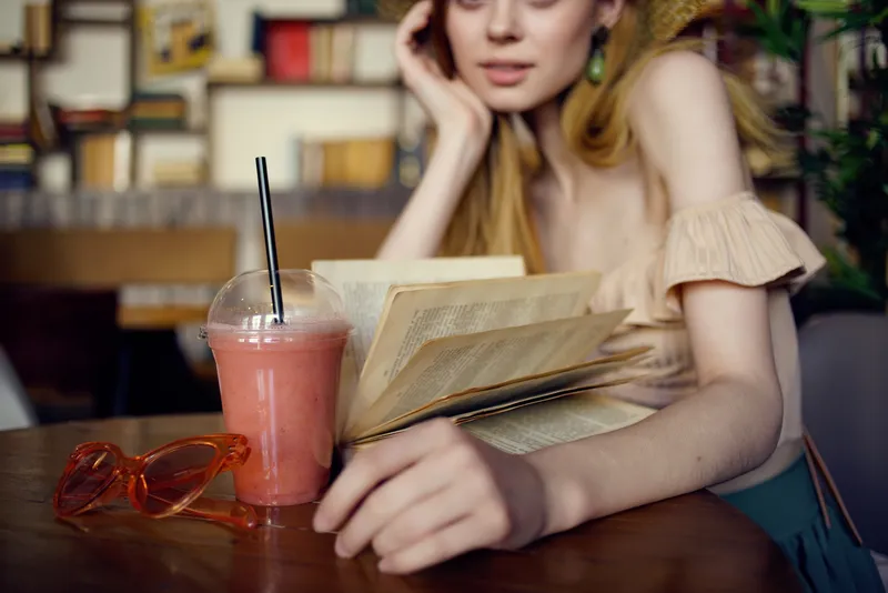 Симпатичная женщина читает книгу в кафе