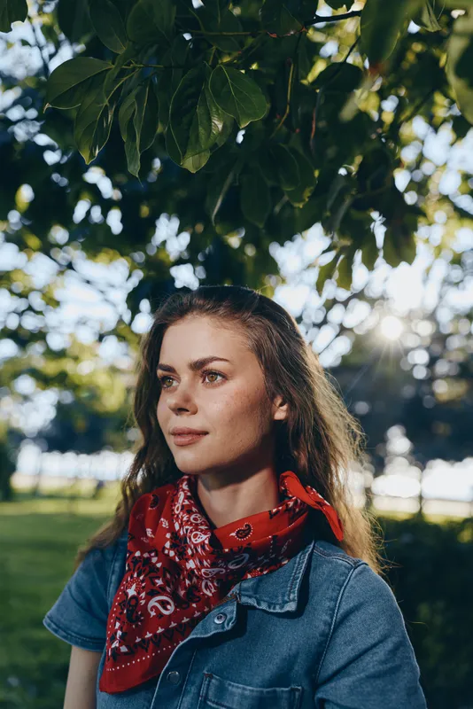 lifestyle woman in modern boho-western denim street style wearing red bandana outdoors with natural sunlight and film color effect creating warm mood