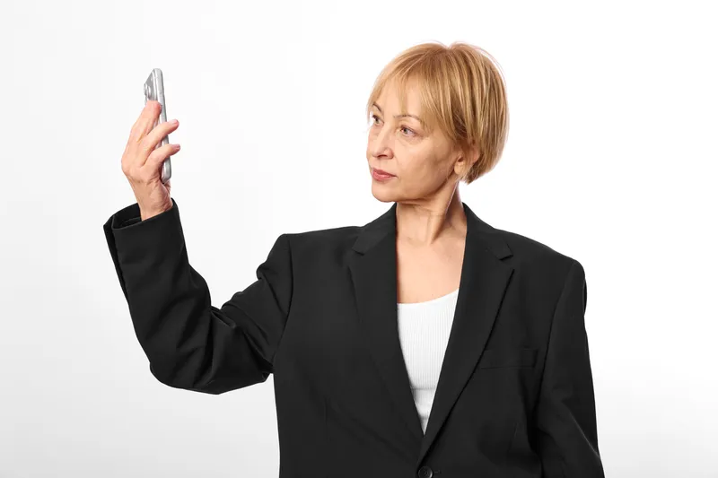 Woman holding smartphone, business portrait on white studio background, businesswoman looking sideways, communication technology concept, calm expression