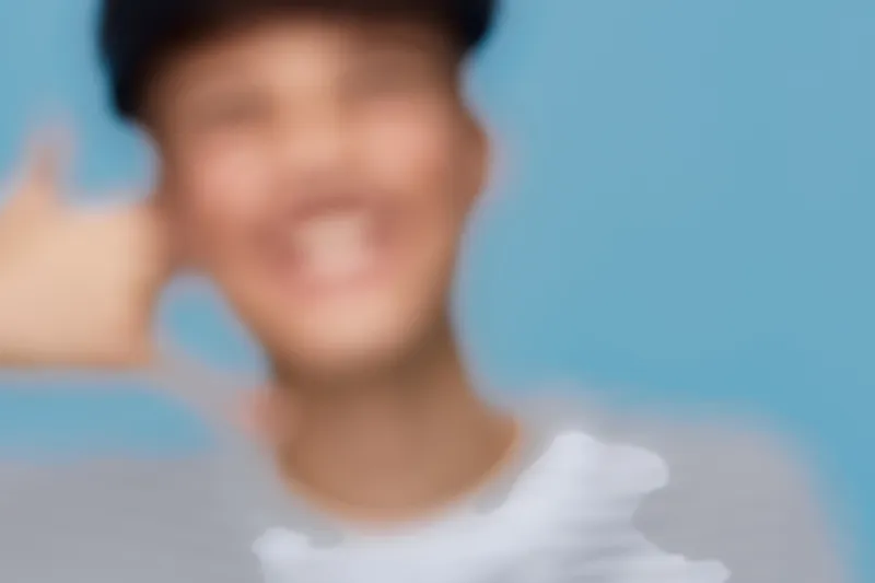 blurred man making call me hand gesture in casual clothes with cheerful smile on blue background, informal communication and positive emotion concept