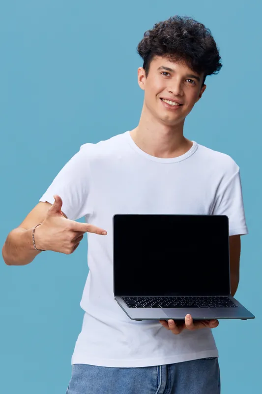 young man holding laptop smiling, casual clothing, blue background, technology concept, happy expression, digital device, isolated studio shot