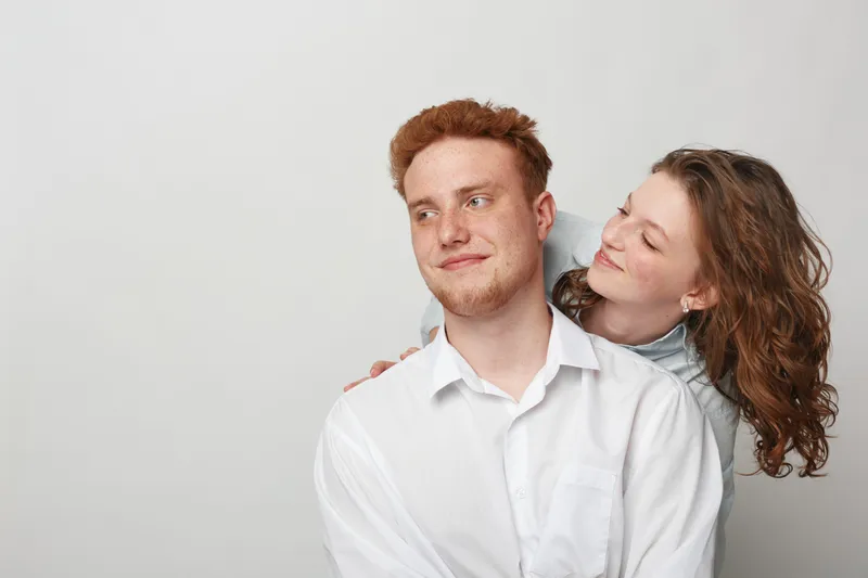 Young couple with red hair and curly hair in casual clothes smiling and looking at each other on white background. Concept of love, relationship, and happiness together.