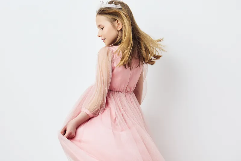 A joyful young girl in a pink tulle dress twirling gracefully, capturing the essence of childhood joy and innocence in a minimalist, bright studio setting