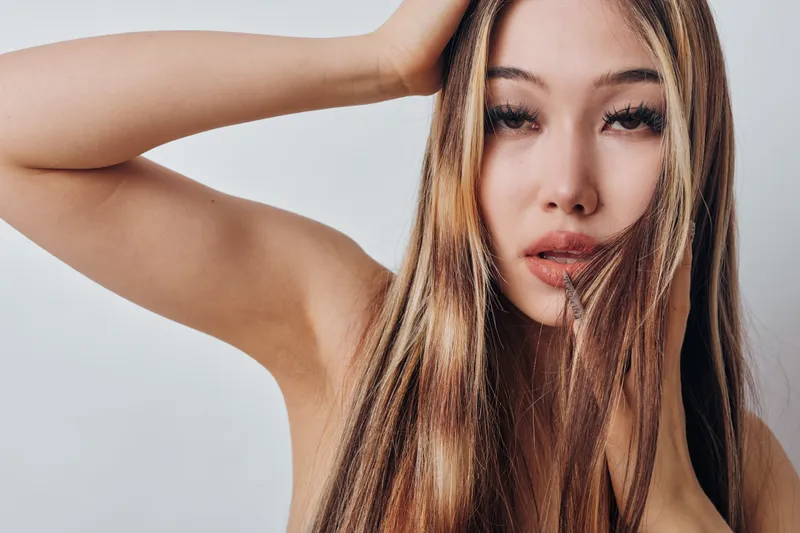 Young woman with long straight hair posing with hand on head against white background. Beauty, fashion, and natural look in closeup portrait style.