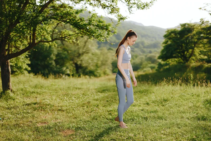 Young woman in activewear practicing yoga in a serene nature background, embodying wellness and vitality in a vibrant green setting