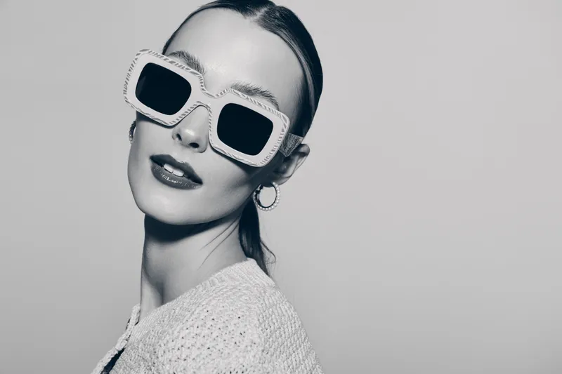 Stylish white woman with fair skin wears oversized sunglasses and knitted top in studio. Concept of fashion, elegance, and modern accessories for women.