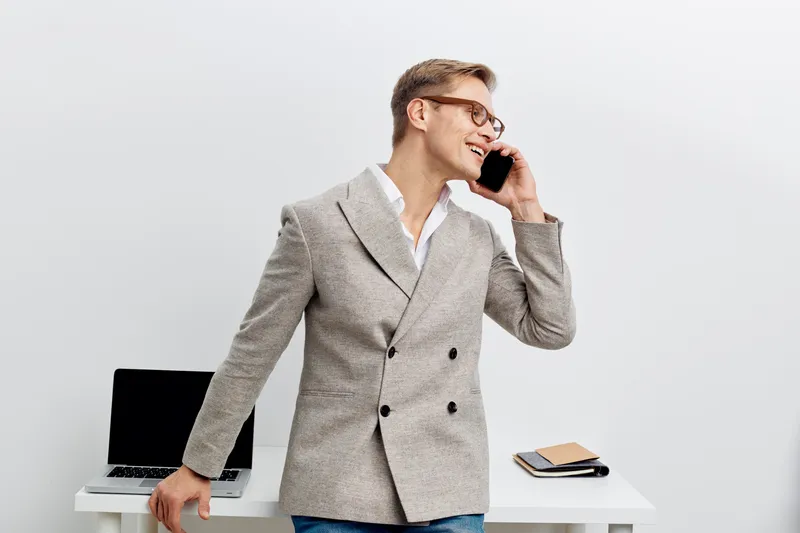 smiling man talking smartphone workspace laptop white background business casual communication concept