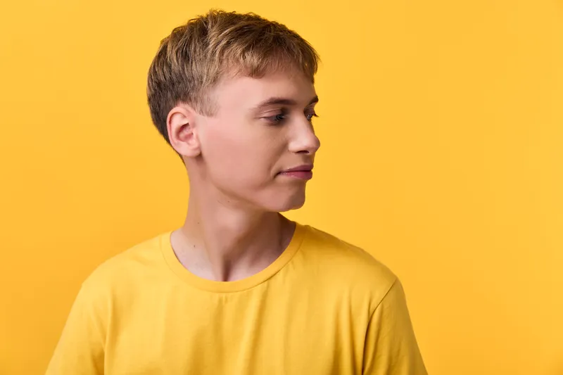 Young man in a yellow shirt, captured in a clean studio with soft lighting, calm expression and side profile against a bright yellow backdrop, ideal for fashion and lifestyle visuals
